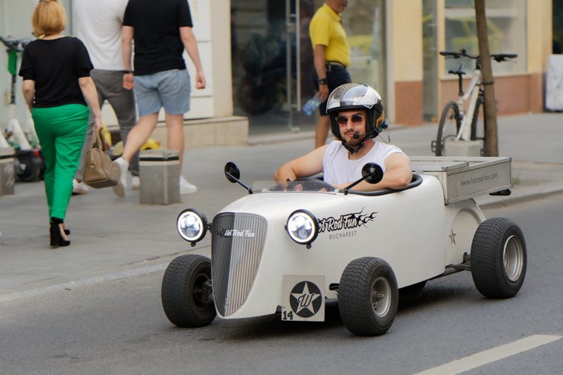 4 - Happy man in a mini vehicle of a guided city tour experience featuring miniature white Hot Rod vehicles